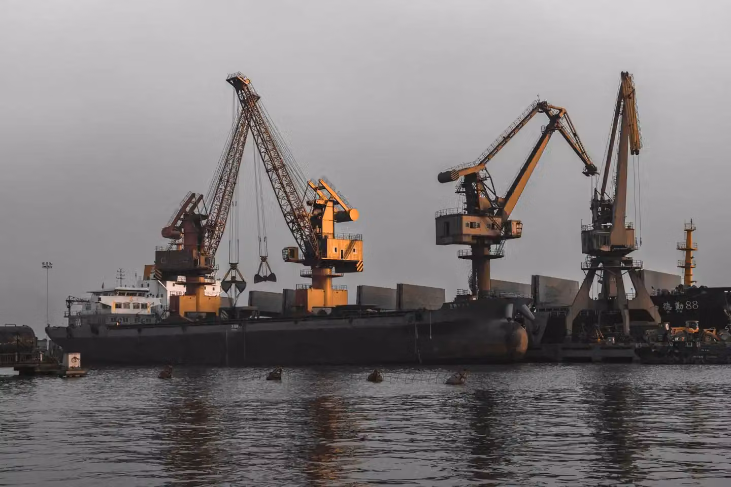 Dockside cargo cranes and industrial vessels alongside a working port