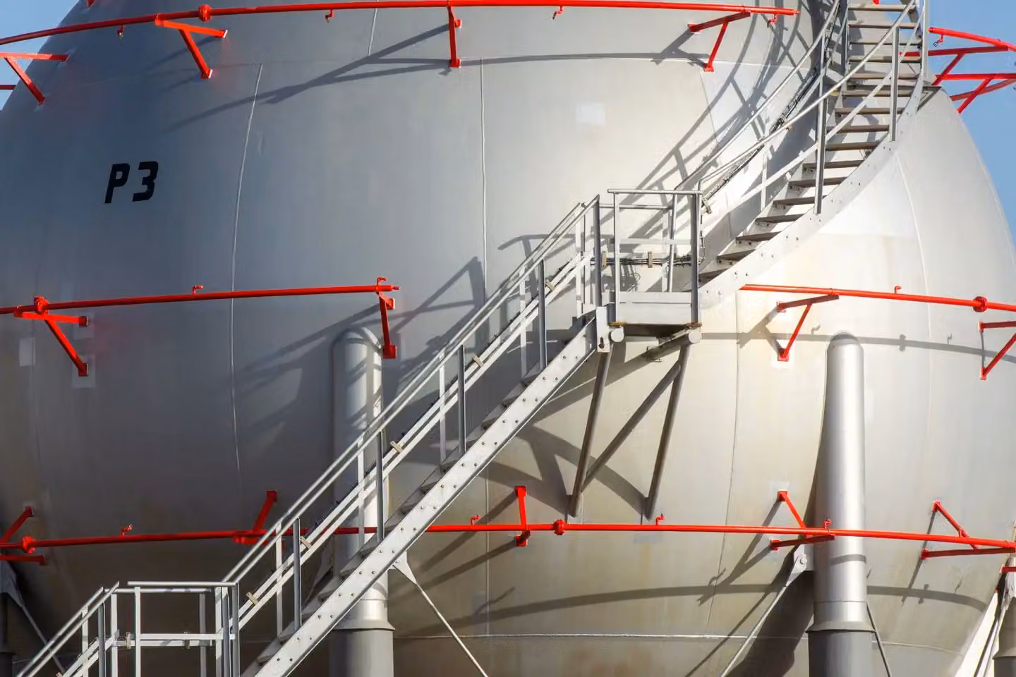 Large industrial storage tank with metal staircase and red railings, symbolizing progress.