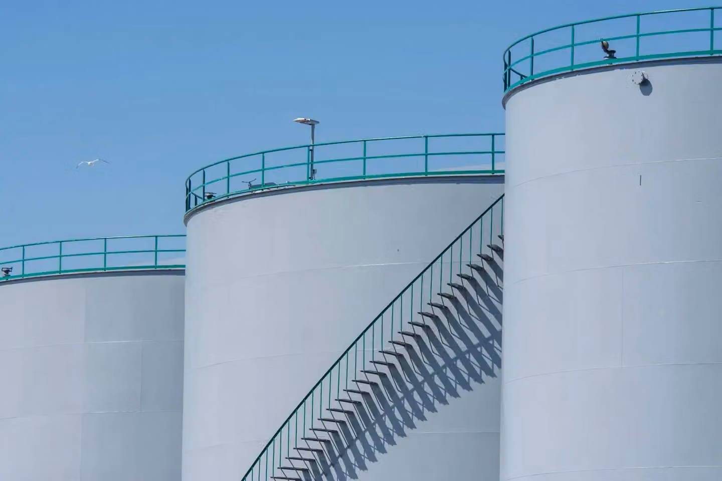Industrial storage tanks with metal stairways under a clear blue sky, highlighting industrial architecture.