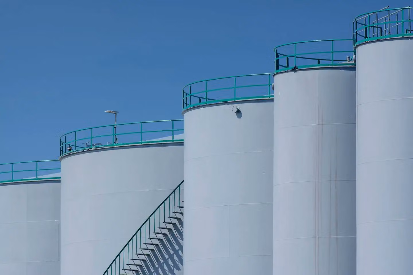 Large industrial storage tanks with green railings against a clear blue sky.