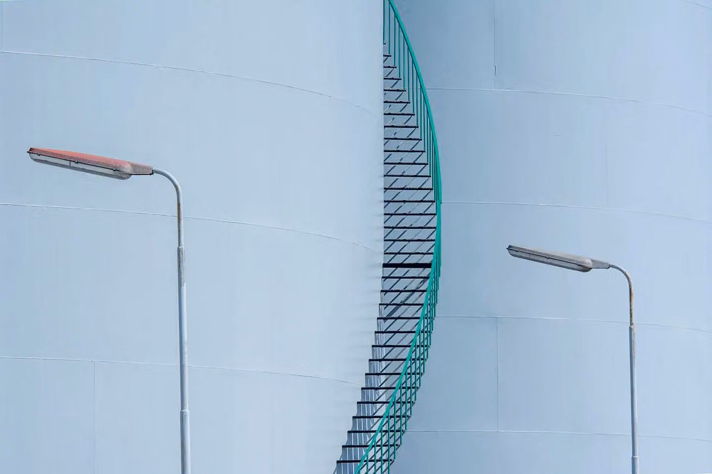Minimalist view of industrial tanks with a staircase and lampposts.