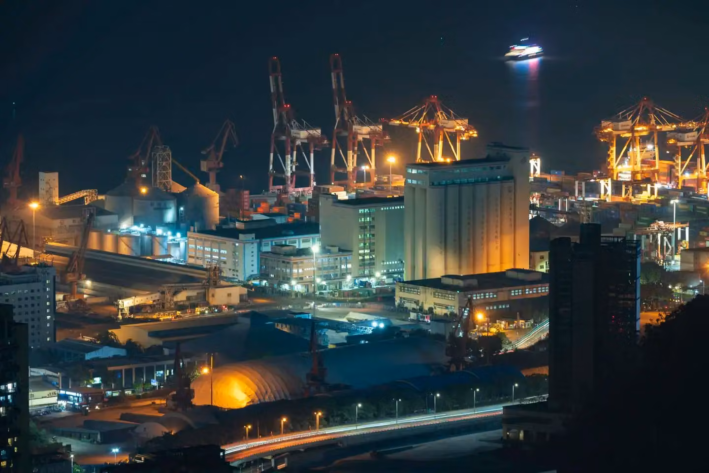 Aerial nighttime view of a vibrant port with illuminated cranes and buildings.